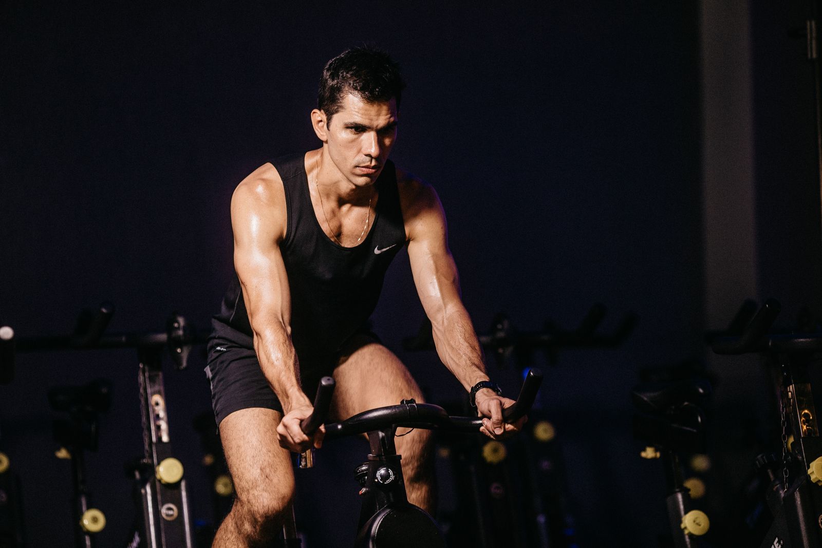 Man i svart linne trampar hårt på en spinningcykel på ett gym, svettig och koncentrerad