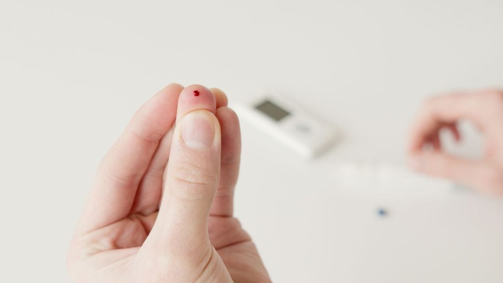 Finger med en droppe blod framför en blodsockermätare