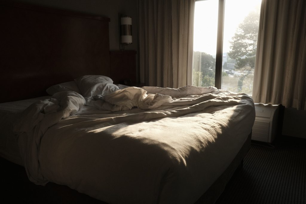 Obäddad säng i ett sovrum där tidigt morgonljus faller in genom fönstret