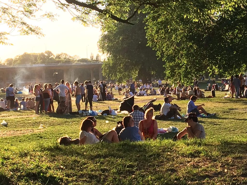 Människor sitter och ligger i gräset i Rålambshovsparken en sommarkväll, med Västerbron i bakgrunden.
