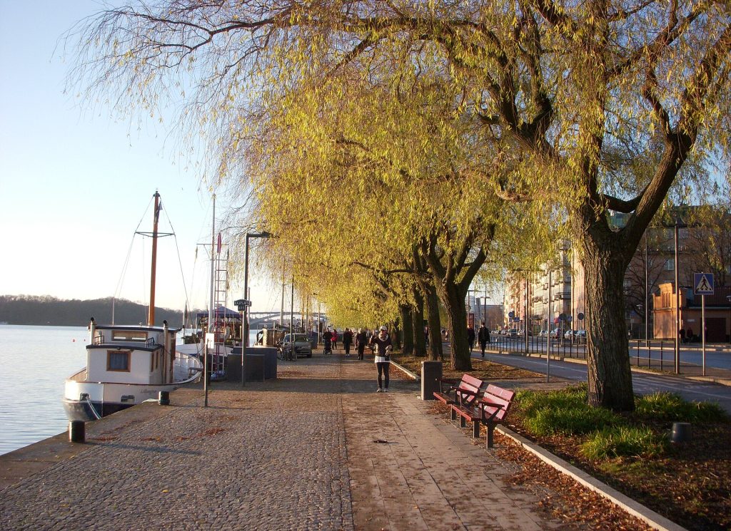 Kajpromenaden längs Norr Mälarstrand med pilträd och röda bänkar, Västerbron i bakgrunden