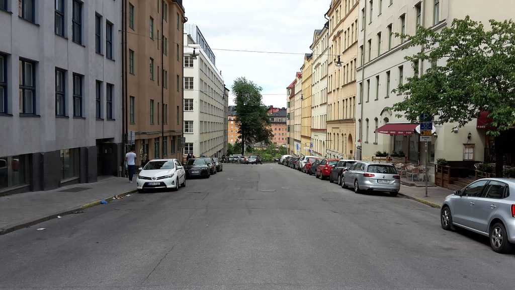 Fridhemsgatan norrut med bostadshus, parkerade bilar och en uteservering under röd markis
