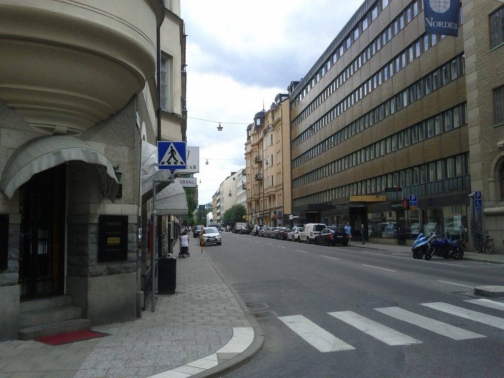 Hantverkargatan på Kungsholmen med restaurangskylt och markiser till vänster och parkerade bilar längs gatan