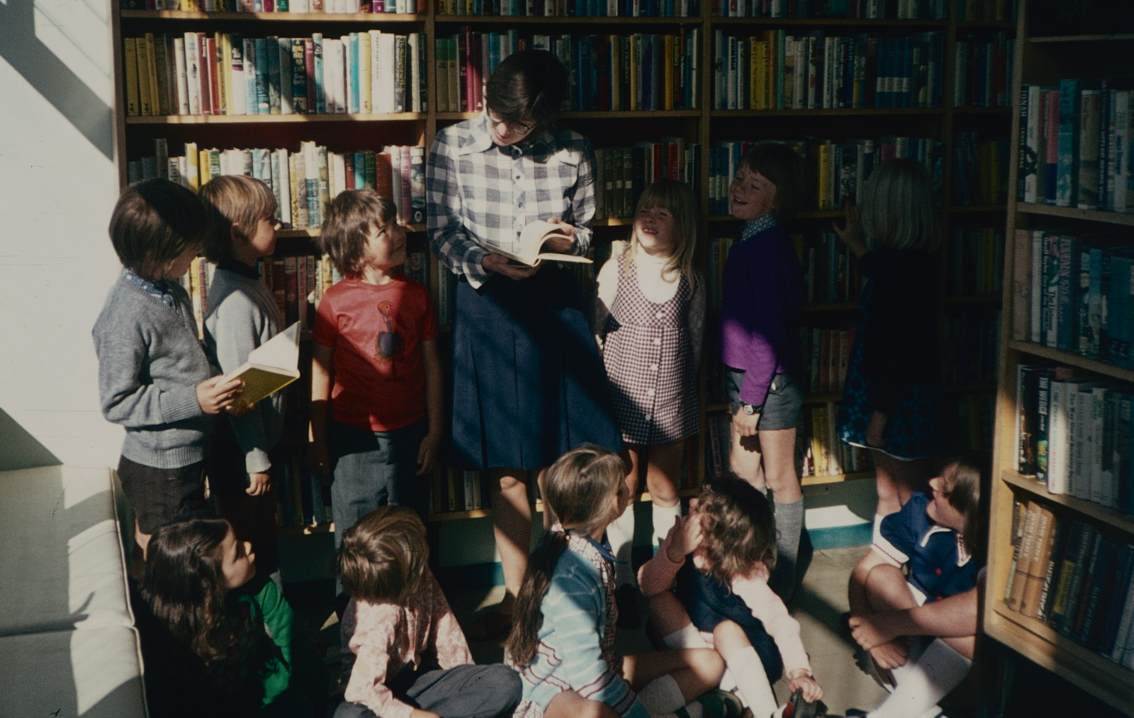 En vuxen läser högt för en grupp barn framför bokhyllorna i ett bibliotek