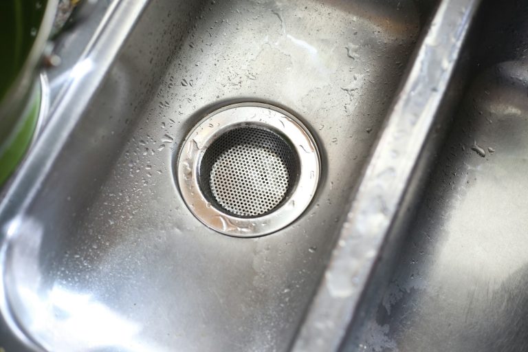 Närbild på en rostfri köksvask med vattendroppar och avloppssil