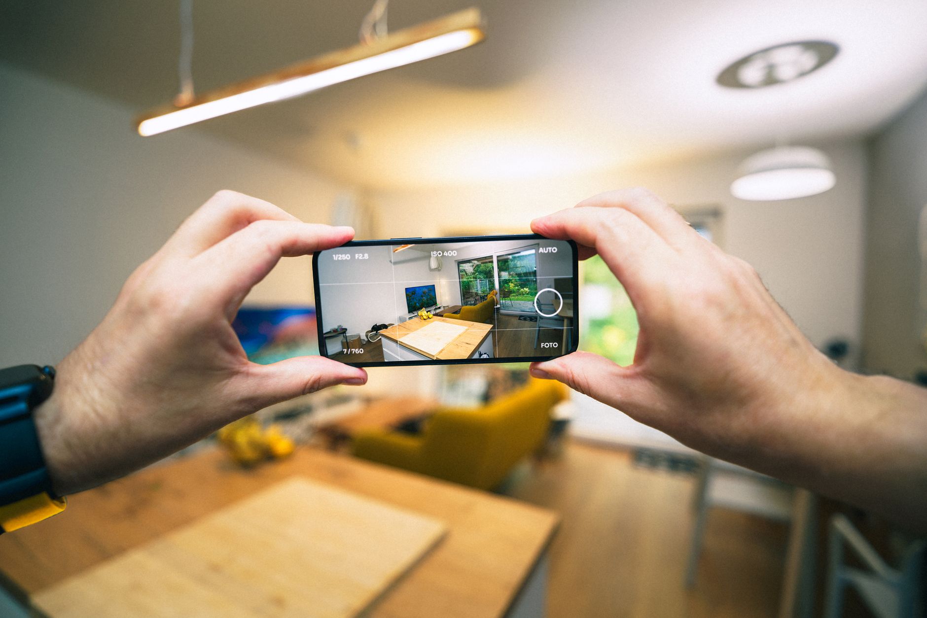 Två händer håller en mobiltelefon och fotograferar ett vardagsrum genom kameraappen