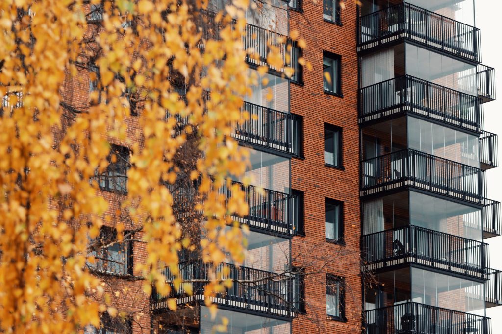 Flerbostadshus i rött tegel med inglasade balkonger bakom gula höstlöv