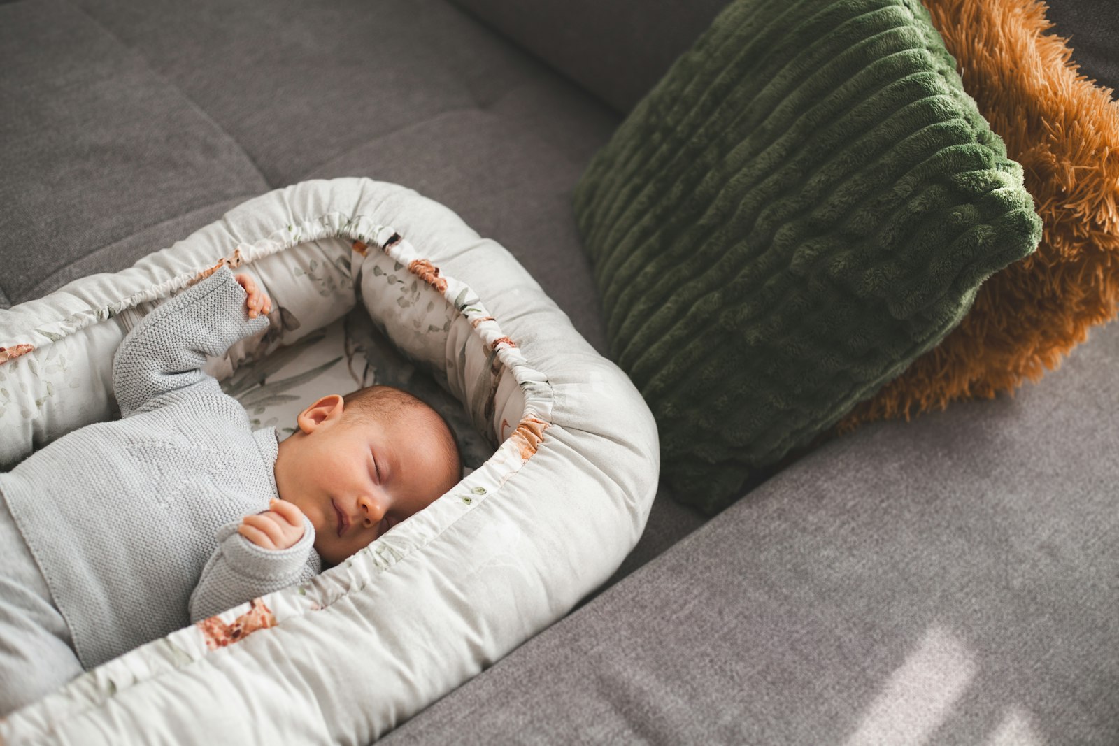 Ett spädbarn ligger på rygg i ett mjukt babynest med kantstöd