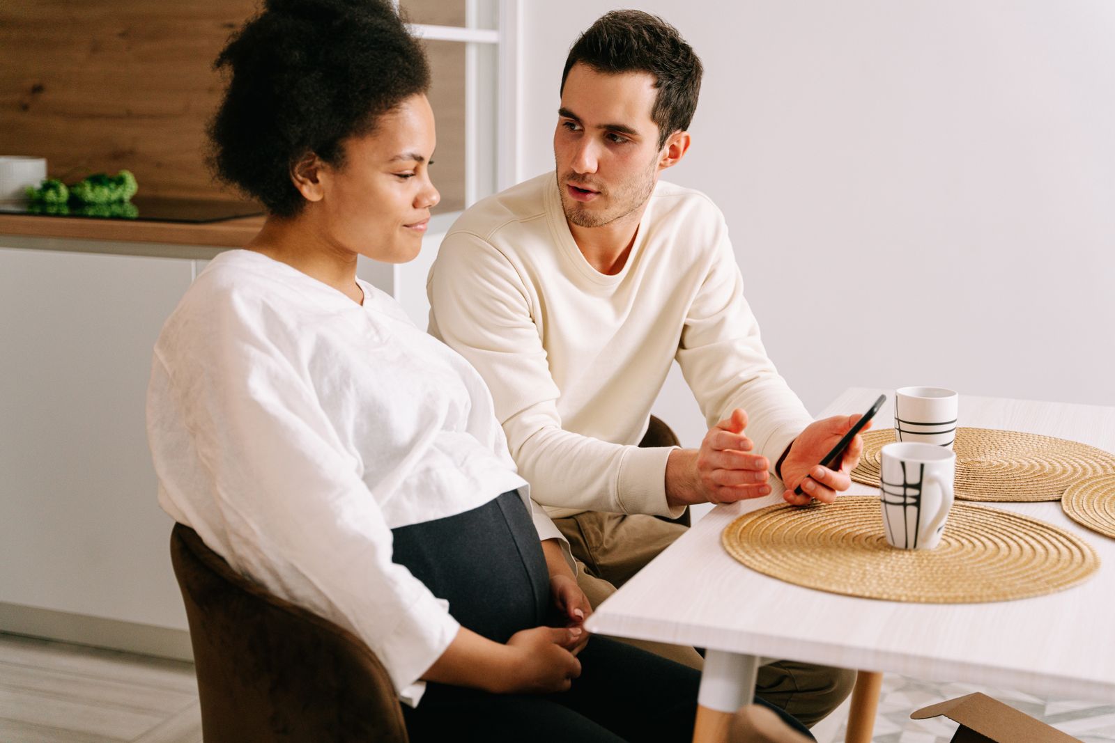 Gravid person och partner sitter vid köksbordet och går igenom planeringen i en mobil