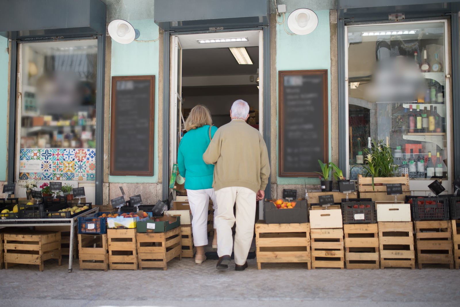 Par på väg in i en lokal närbutik med grönsakslådor vid entrén
