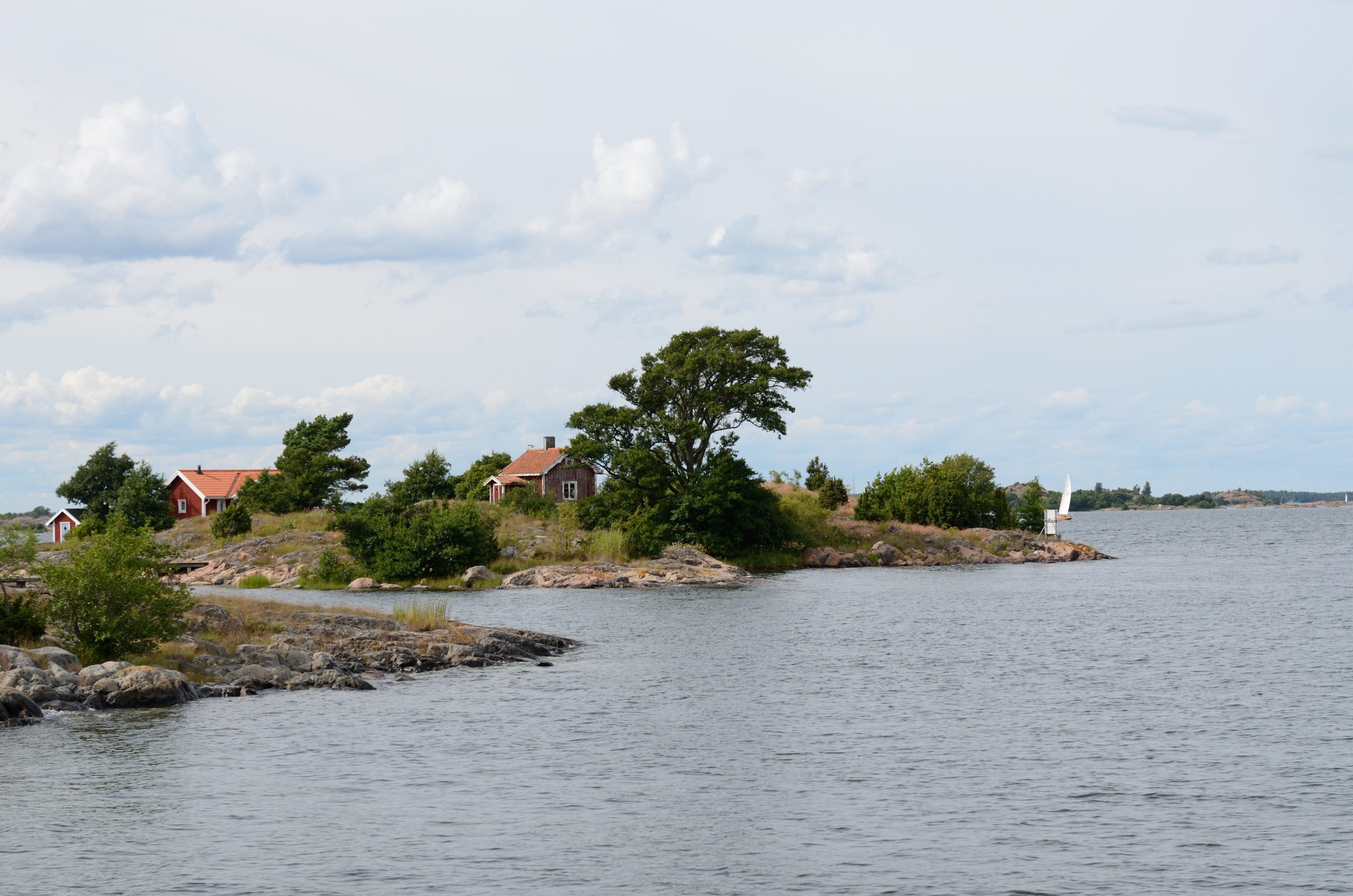 Låga klipphällar med röda skärgårdsstugor i Sankt Anna skärgård, med öppet vatten och fler öar i bakgrunden