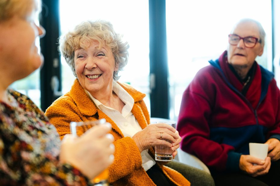Tre äldre vänner sitter tillsammans, samtalar och skrattar över var sitt glas