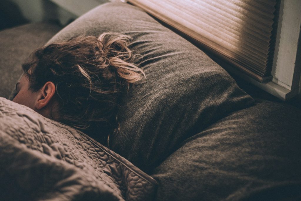 Person som sover i en säng med morgonljus genom persiennerna