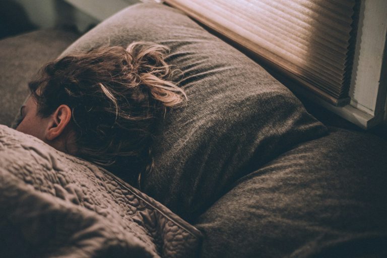 Person som sover i en säng med morgonljus genom persiennerna