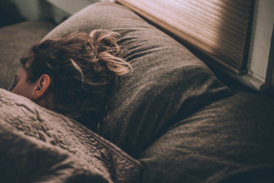 Person som sover i en säng med morgonljus genom persiennerna