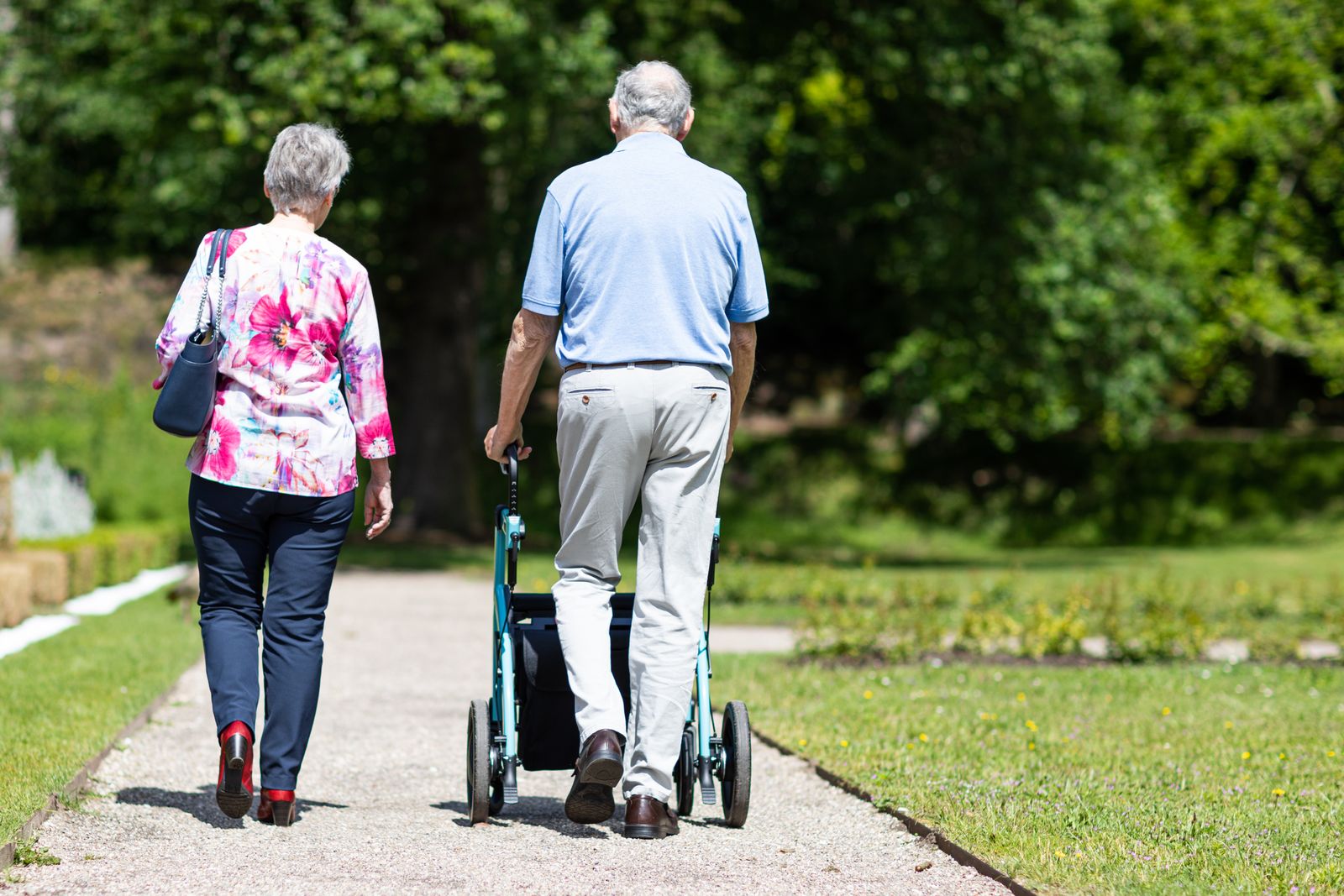 Äldre man med rollator promenerar tillsammans med en kvinna i en park