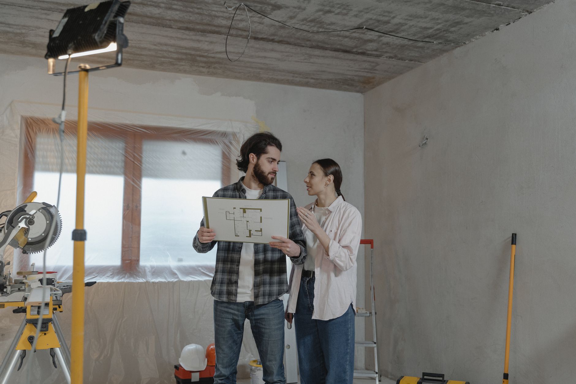 Två personer studerar en planritning i ett rum under renovering