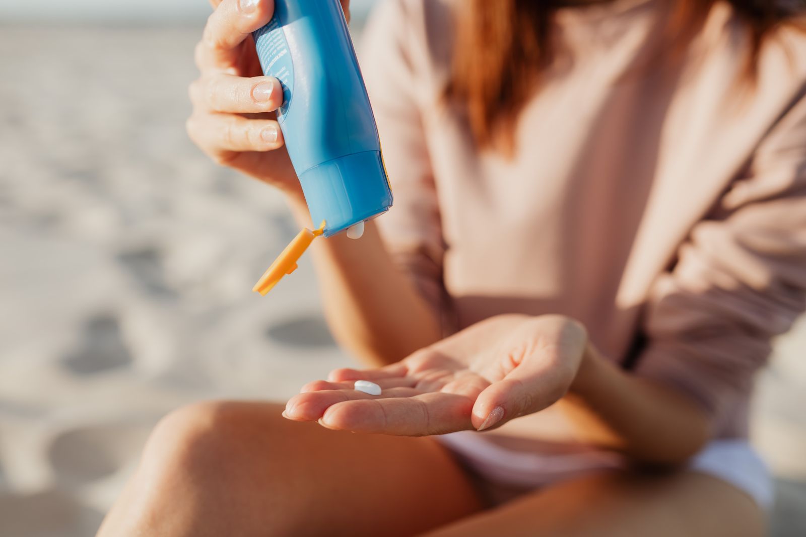 Person doserar solskyddskräm i handen på stranden, skydd mot UV