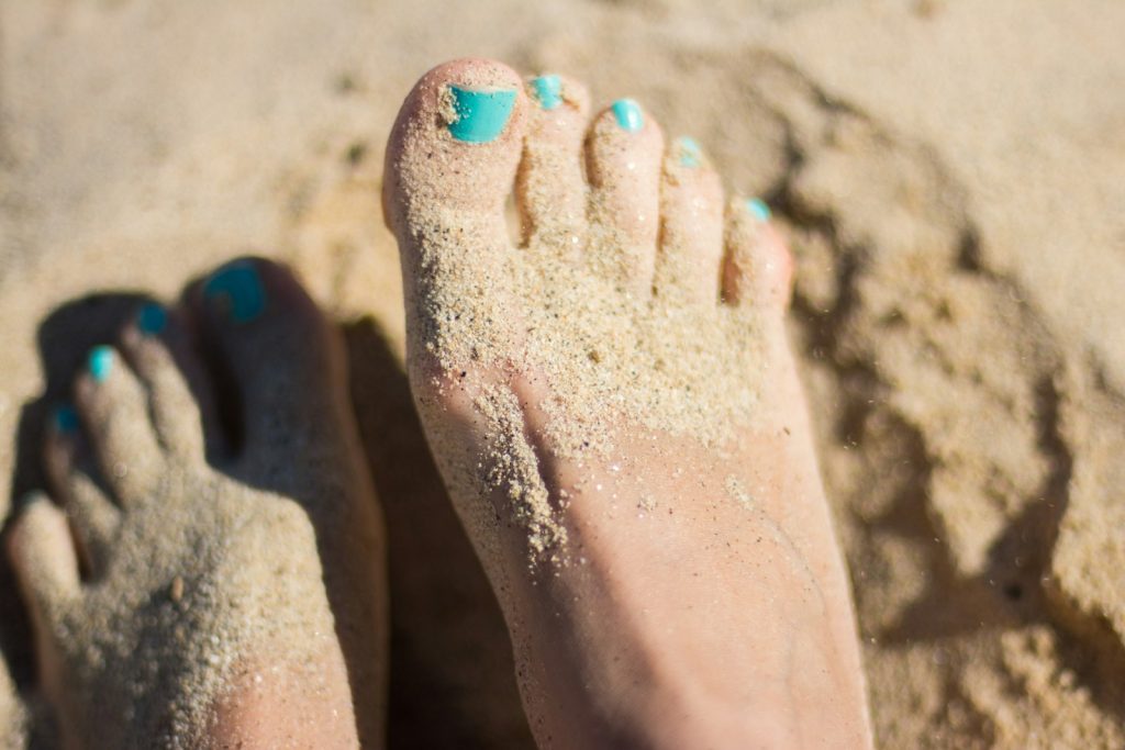 Fötter med turkos nagellack i sanden på en strand