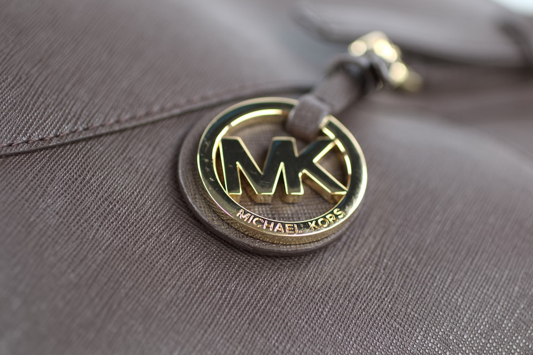 Närbild på den runda guldfärgade MK-berlocken med texten MICHAEL KORS på en väska i Saffiano-läder