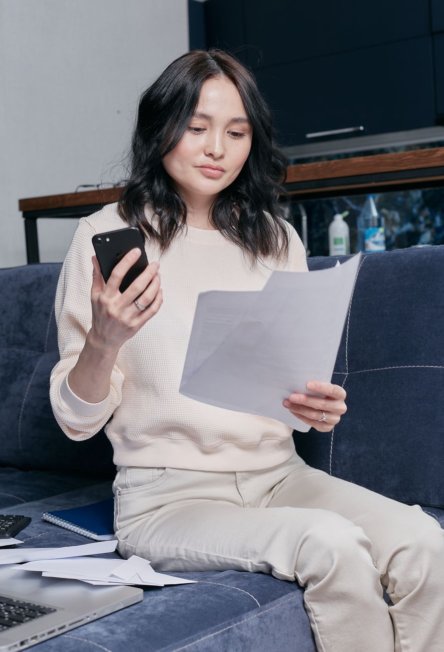 Kvinna i soffan läser ett brev med mobilen i handen