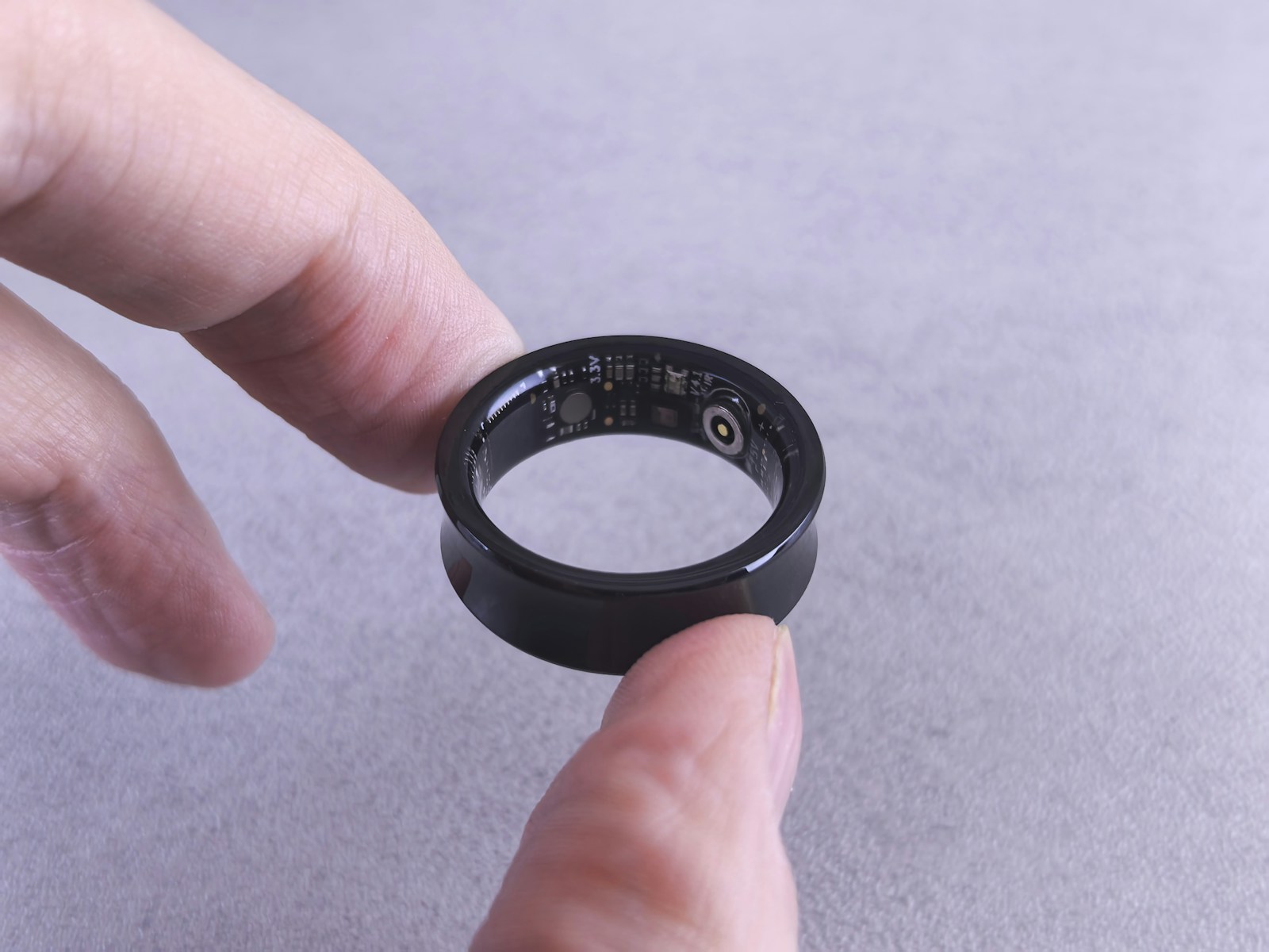 Black smart ring held between two fingertips, its internal sensors and circuit board visible