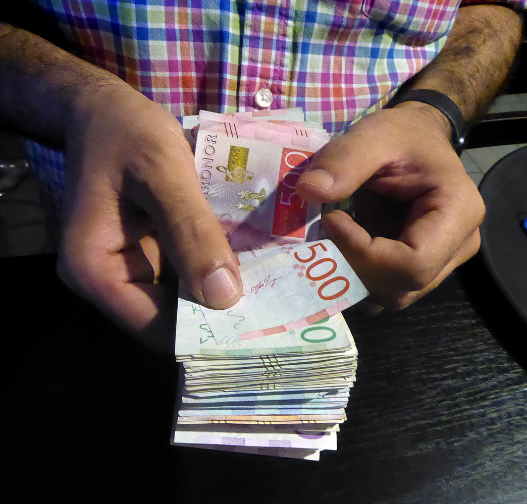 Person räknar en bunt svenska sedlar, bland annat 500-kronorssedlar