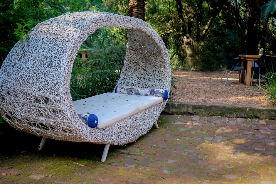 Rottingdaybed med lösa dynor i en skuggig trädgård