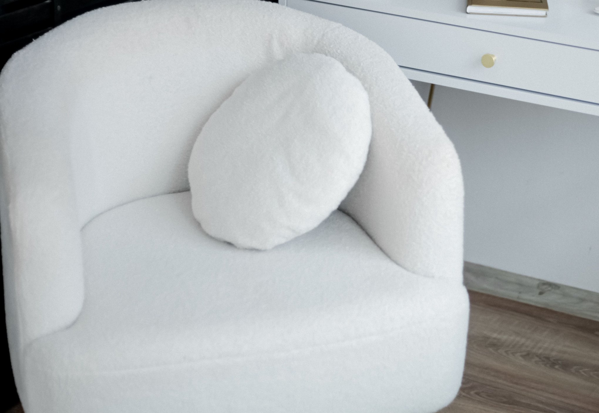 Vit fåtölj klädd i luddigt teddytyg med en rund kudde i samma tyg