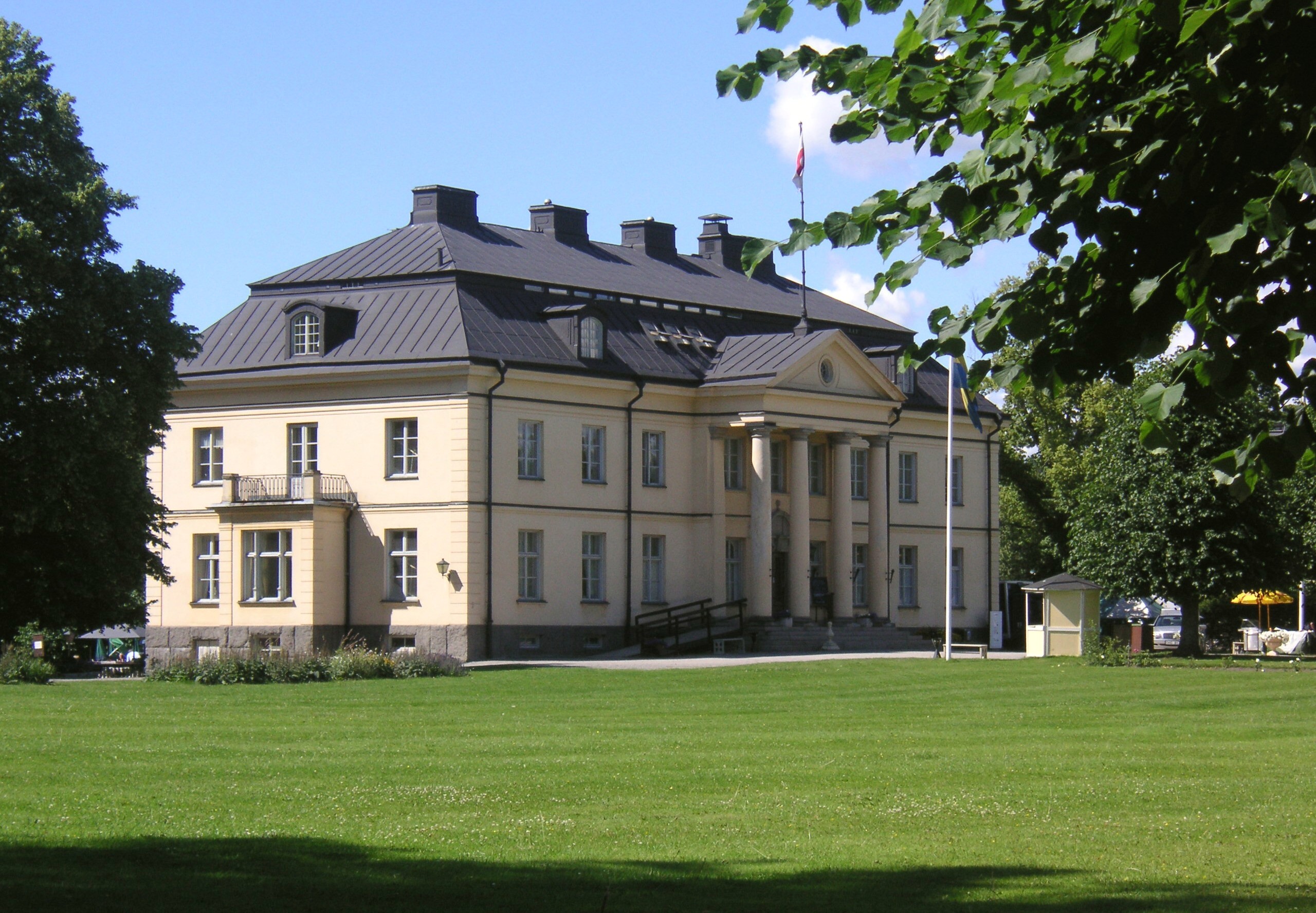 Hågelby herrgård med gul huvudbyggnad, pelare och park