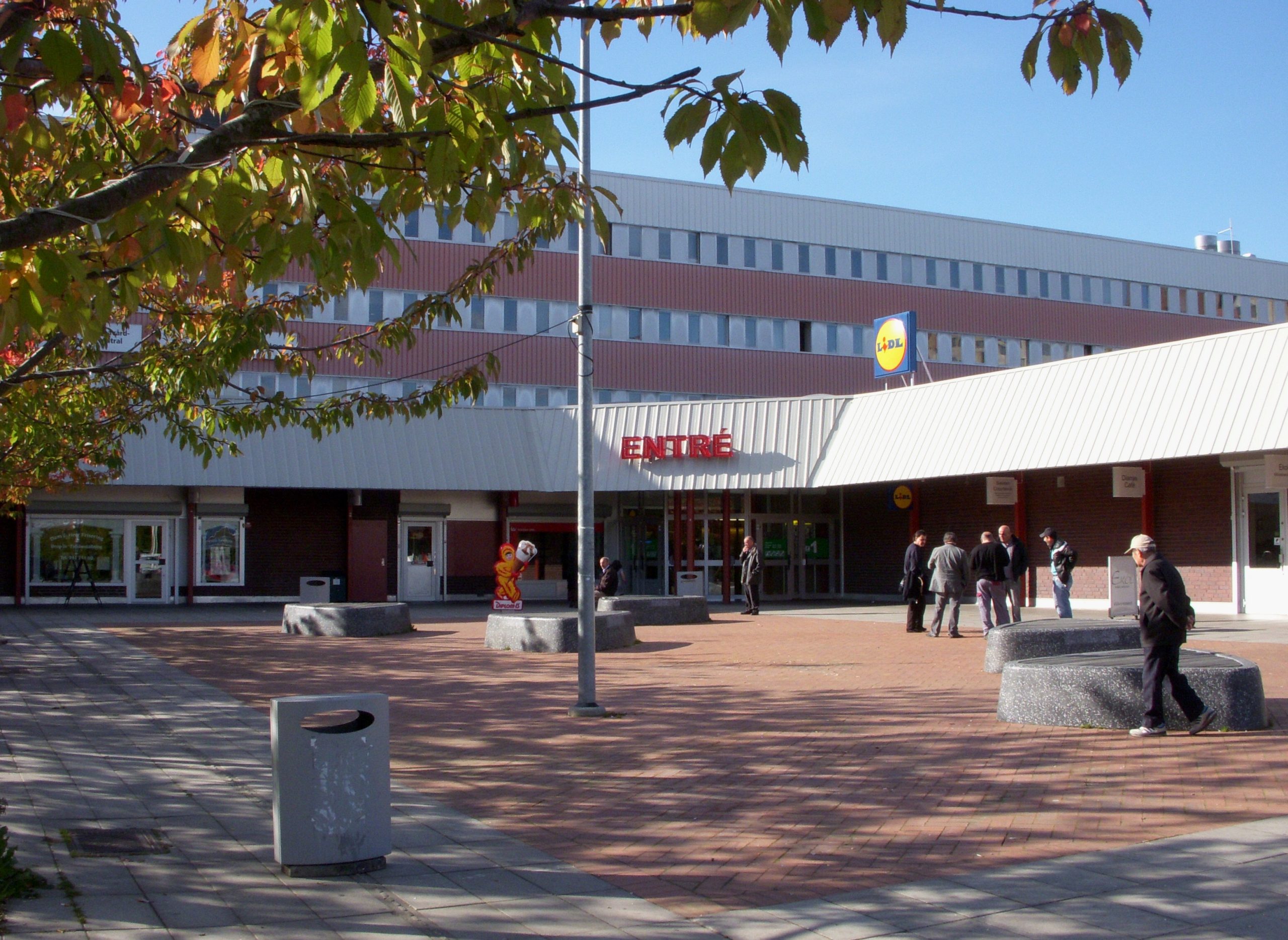 Entrén till Fittja centrum en höstdag, med tegelfasad och besökare på torget