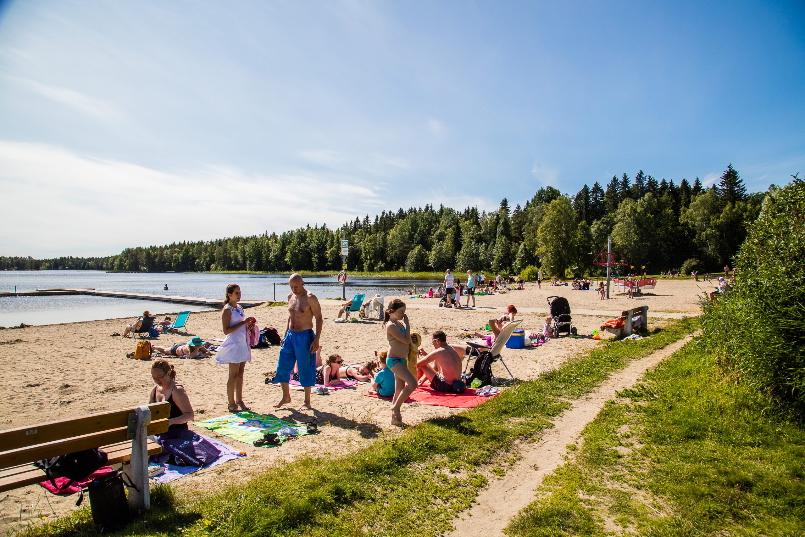 Solig badstrand vid Nydalasjon med badande och skog