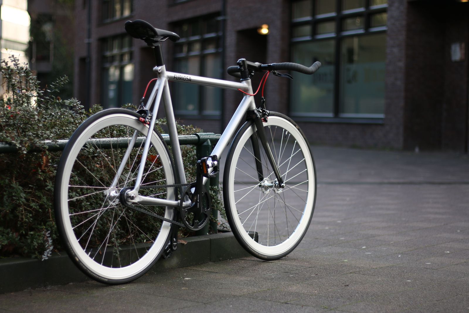 Vit fixie med fast drev lutad mot betongvägg i stadsmiljö