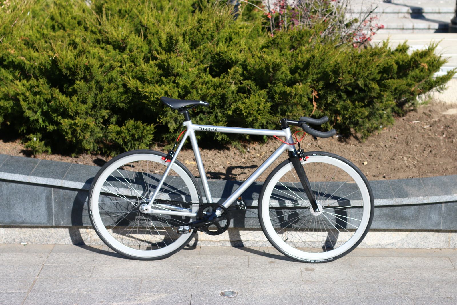 Avskalad silverfärgad fixie med bullhorn-styre lutad mot kantsten