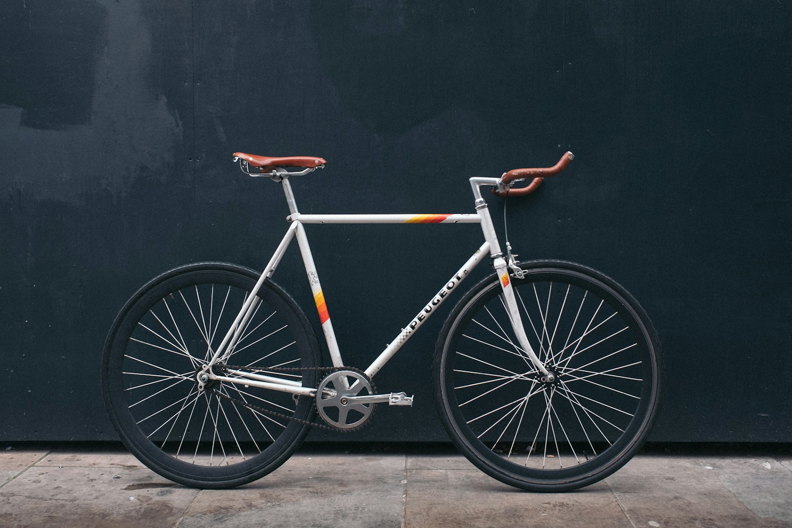 En fixie med enkel drivlina och banstyre lutad mot en mörk vägg