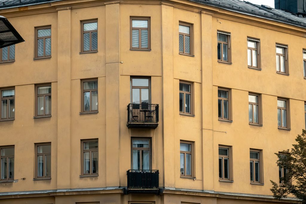 Fasaden på ett klassiskt gulputsat flerbostadshus i Stockholm med spröjsade fönster och små balkonger