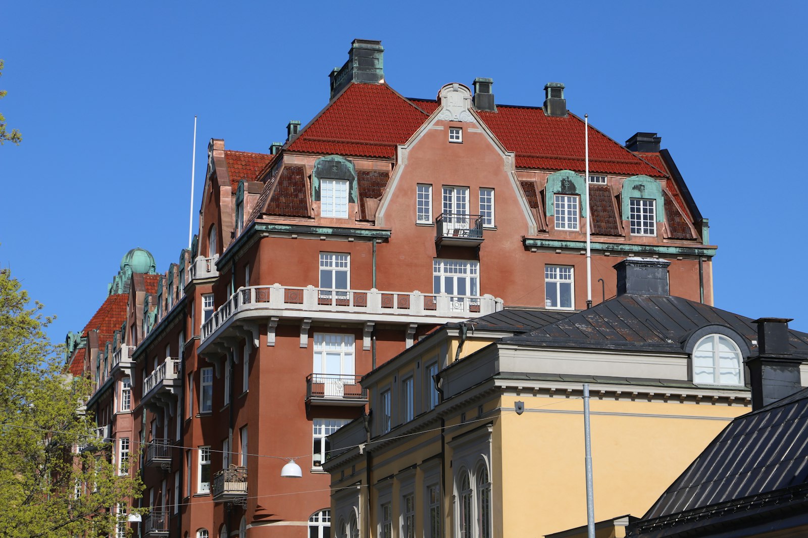 Tegelrött sekelskifteshus med takkupor och kopparplåtar mot blå himmel