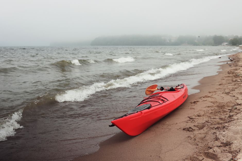 Röd kajak liggande obevakad på en strand med vågor